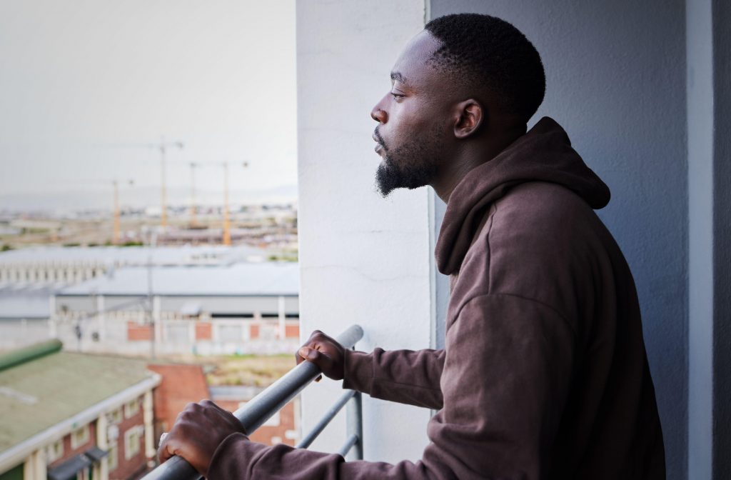 2K1DFKX Depressed, sad and thinking man with mental health problem on balcony, planning idea while in apartment with anxiety and burnout from depression. Fail